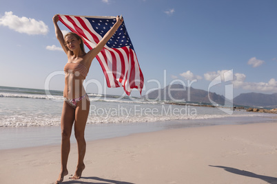 Young woman holding waving American flag at beach