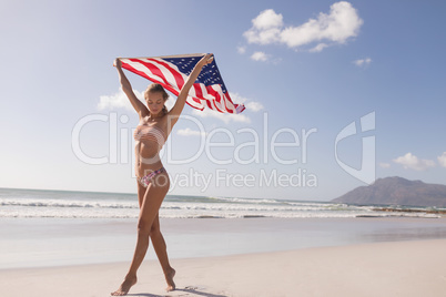 Young woman holding waving American flag at beach