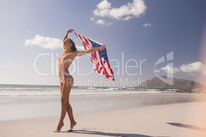 Young woman holding waving American flag at beach