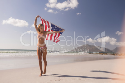 Young woman holding waving American flag at beach