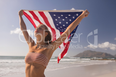 Young woman holding waving American flag at beach