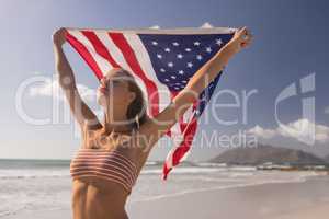 Young woman holding waving American flag at beach