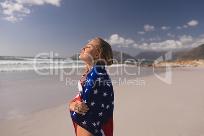 Young woman wrapped in American flag at beach