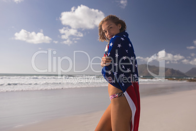 Young woman wrapped in American flag at beach