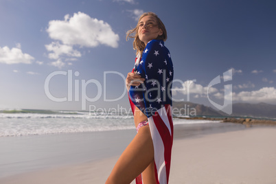 Young woman wrapped in American flag at beach