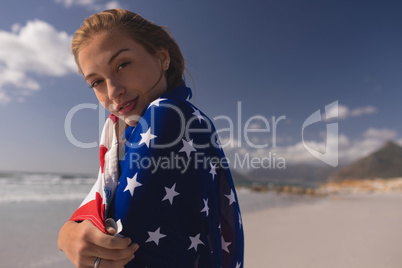 Young woman wrapped in American flag at beach