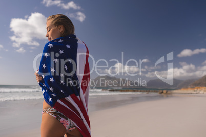 Young woman wrapped in American flag at beach