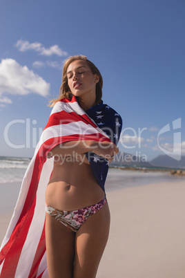 Young woman wrapped in American flag at beach