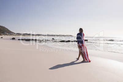 Young woman wrapped in American flag at beach