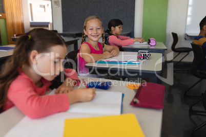 Schoolgirl looking at camera while studying in classroom