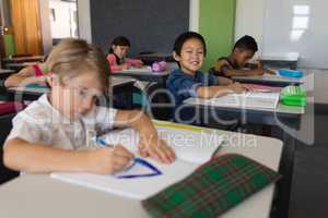 Schoolboy looking at camera while studying in classroom
