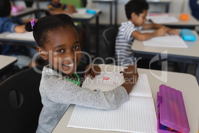 Schoolgirl looking at camera while studying in classroom