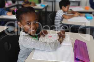 Schoolgirl looking at camera while studying in classroom
