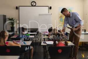 School teacher holding digital tablet and teaching in a classroom