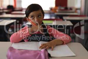 Thoughtful schoolgirl studying in classroom sitting at desks in school