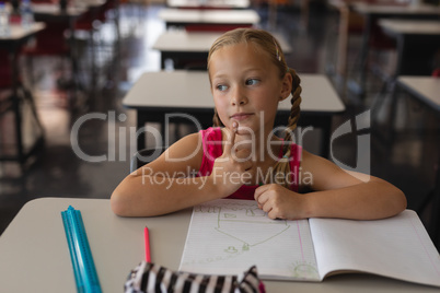 Thoughtful schoolgirl studying in classroom sitting at desks in school