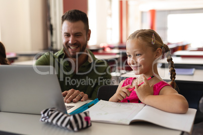 Young school teacher helping girl with study on laptop in classroom