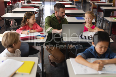 Young school teacher helping girl with study on laptop in classroom