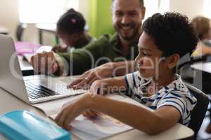 Young school teacher helping boy with study on laptop in classroom