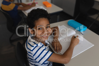 Schoolboy looking at camera while studying in classroom