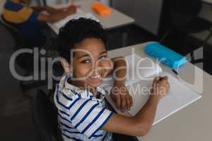 Schoolboy looking at camera while studying in classroom