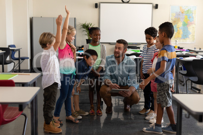 School kids raising hands while teacher teaching