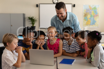 Male teacher teaching kids on laptop in classroom