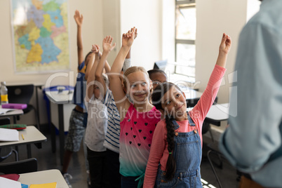 School kids standing in row and raising hand in classroom