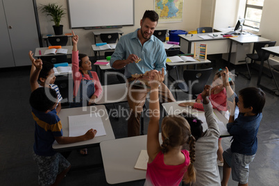 School kids raising hands while teacher teaching in classroom