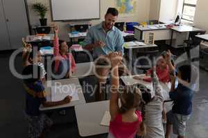 School kids raising hands while teacher teaching in classroom