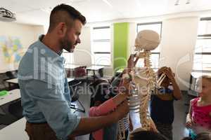Side view of male teacher explaining skeleton model in classroom