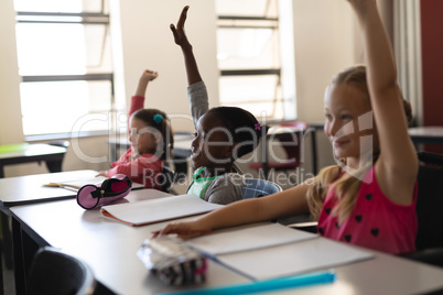 Schoolgirls raising hand in classroom of elementary school