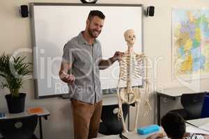 Side view of happy male teacher explaining human skeleton model in classroom