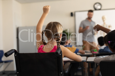 Rear view of disable schoolgirl raising hand in classroom