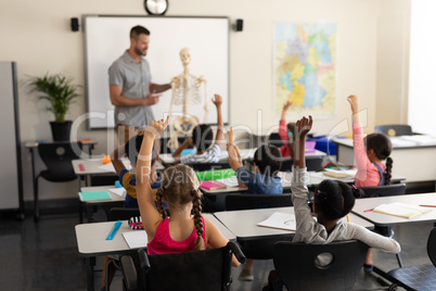 School kids raising hand and sitting at desk in elementary school