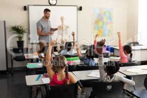 School kids raising hand and sitting at desk in elementary school