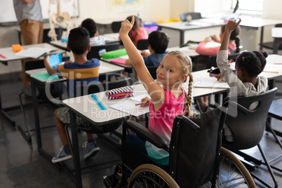 Smiling disable schoolgirl looking at camera and raising hand in classroom