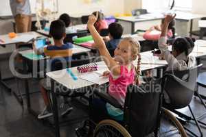 Smiling disable schoolgirl looking at camera and raising hand in classroom
