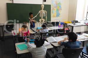 Rear view of schoolboy explaining human skeleton model in classroom