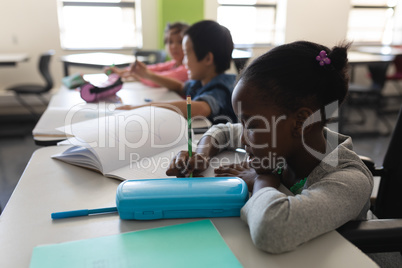 Side view of disable black schoolgirl studying and sitting at desk in classroom