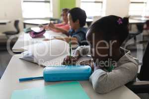 Side view of disable black schoolgirl studying and sitting at desk in classroom