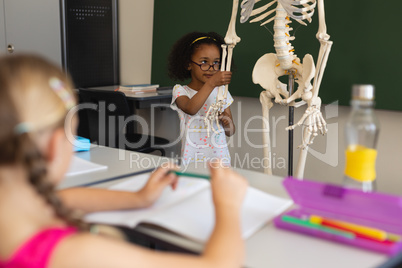 Little schoolgirl explaining human skeleton model in classroom