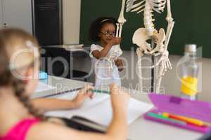 Little schoolgirl explaining human skeleton model in classroom