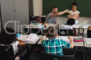 Rear view of schoolkids studying and sitting at desk in classroom