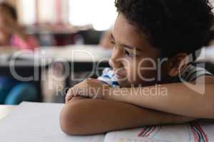 Close-up of thoughtful schoolboy leaning on desk and looking away in classroom