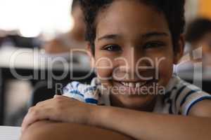 Close-up of happy school boy leaning on desk and looking at camera in classroom