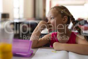 Close-up of thoughtful schoolgirl leaning on desk and looking away in classroom