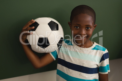 Front view of black schoolboy holding football and looking at camera in classroom