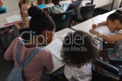 Rear view of schoolgirls studying together at desk in classroom