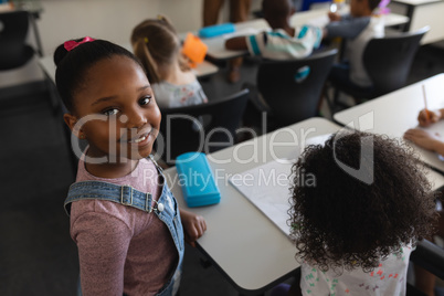 Smiling black schoolgirl standing and looking at camera in classroom